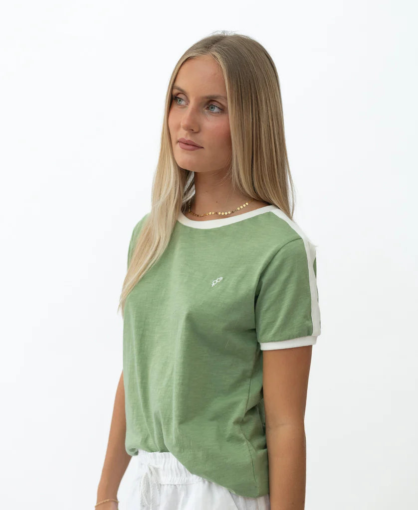 Young woman wearing a green Retro Ringer Tee | Moss with white trim on sleeves and collar standing against a plain white background in a relaxed pose.