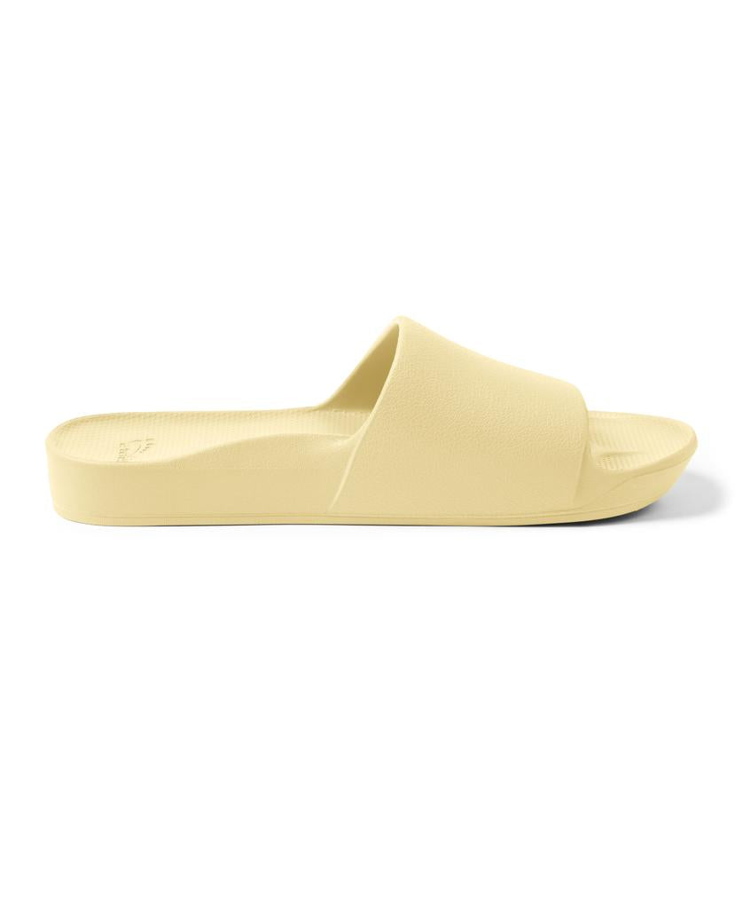 The Archies Archie Slide in Lemon is a light yellow sandal with a thick strap and textured, foot-moulding foam footbed, shown in side profile against a white background.