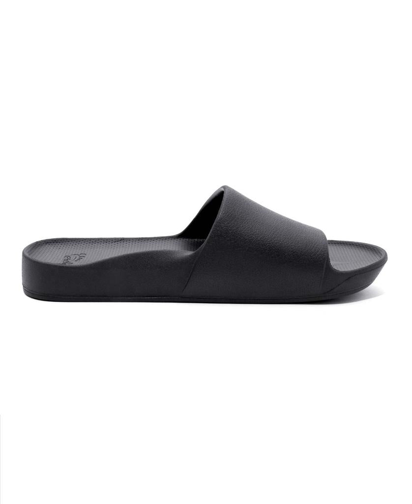 The Archie Slide | Black by Archies is a slip-on sandal featuring a wide strap, flat sole, and open toe, crafted from closed cell foam for comfort. Shown in profile against a white background.