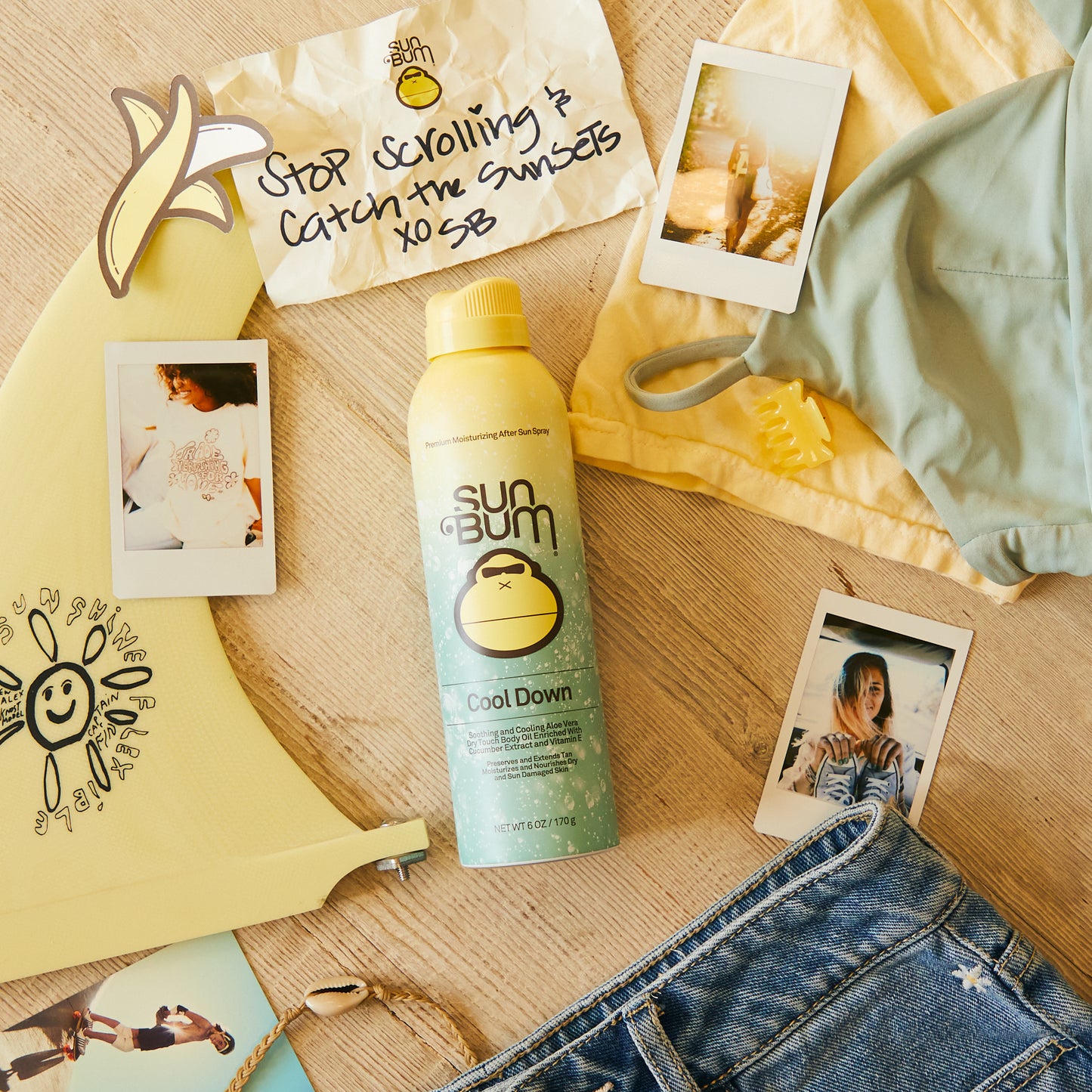 The Sun Bum Aloe Spray | 177ml sits among photos, denim shorts, yellow swim fins, and a green bikini top on wood—ideal for soothing skin with Sun Bum’s non-greasy formula.
