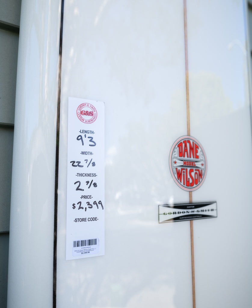 A Gordon & Smith G&S 93 Dane Wilson Polish Finish longboard in white, measuring 9’3” x 22 7/8” x 2 7/8”, is priced at $2,399 and features the Dane Wilson logo.