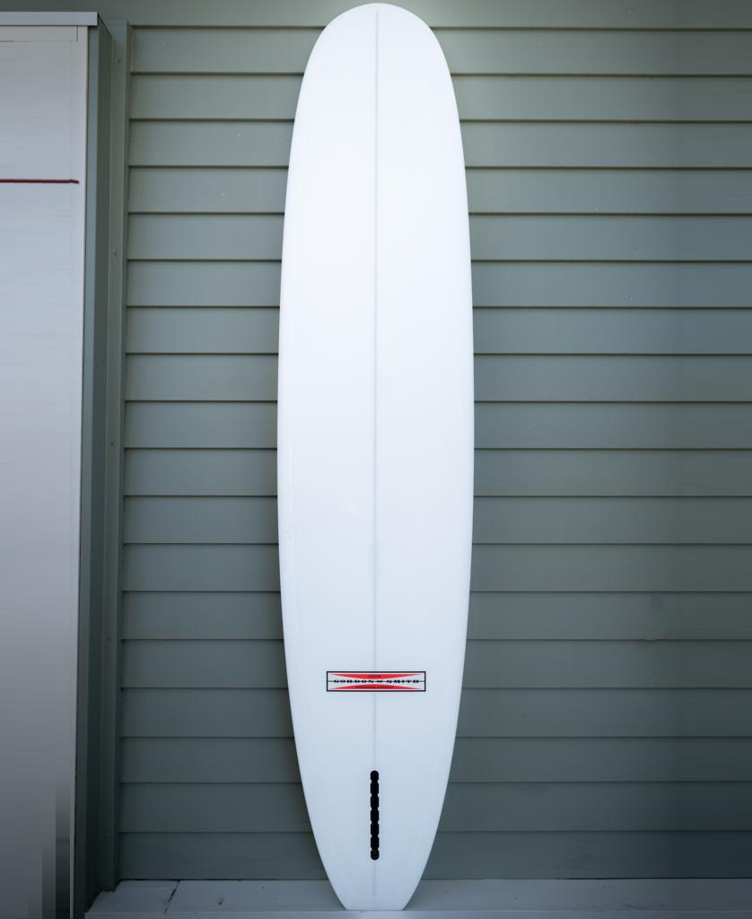 The Gordon & Smith G&S 93 Easy Rider Polish Finish longboard in green/white stands vertically against a grey horizontal slat wall.