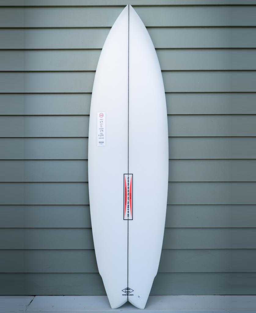 The Gordon & Smith G&S 64 Power Twin Matte Finish | White, featuring a pointed nose and slightly rounded tail, stands upright against a gray paneled wall.
