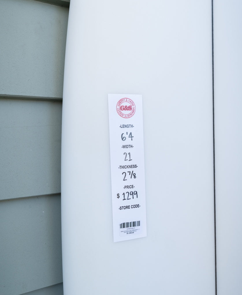A white Gordon & Smith G&S 64 Power Twin Matte Finish board (64 length, 21 width, 2 7/8 thickness) priced at $1,299 leans against the wall—perfect for quality seekers or surf freight specialists.