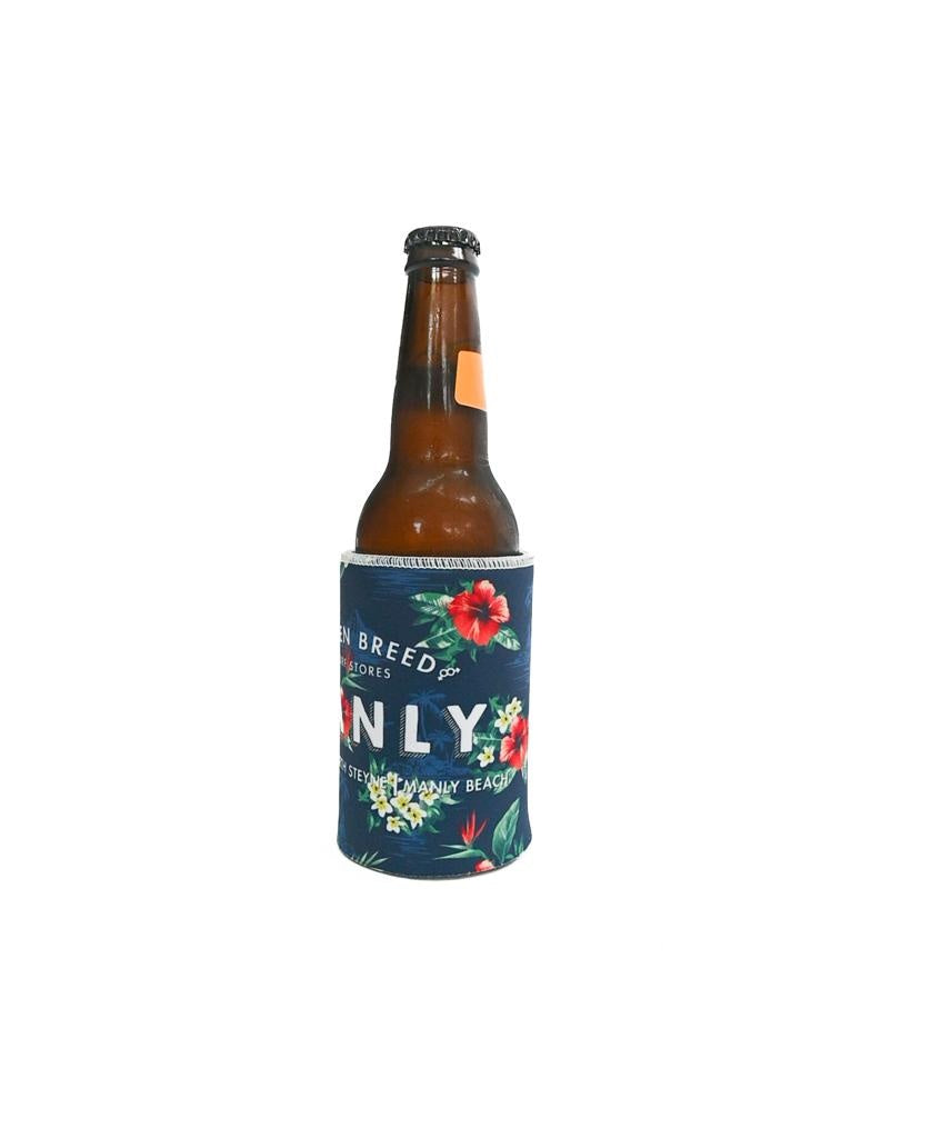 A brown glass beer bottle stands upright in a Golden Breed Manly Stubby Aloha | Dark Navy holder, featuring a floral pattern on blue neoprene, with partial text visible against a white background.