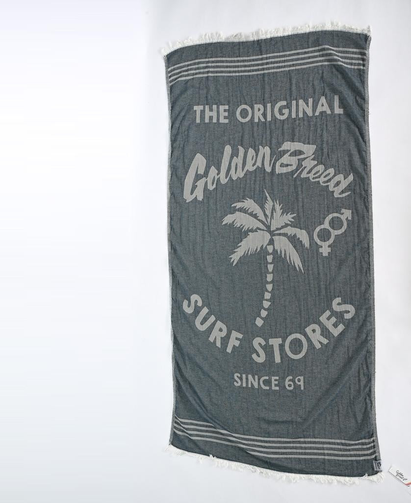 The Golden Breed GB Otto Towel in Navy is made from soft Turkish cotton, features fringe edges, a palm tree graphic, and the text: The Original Golden Breed Surf Stores Since 69.
