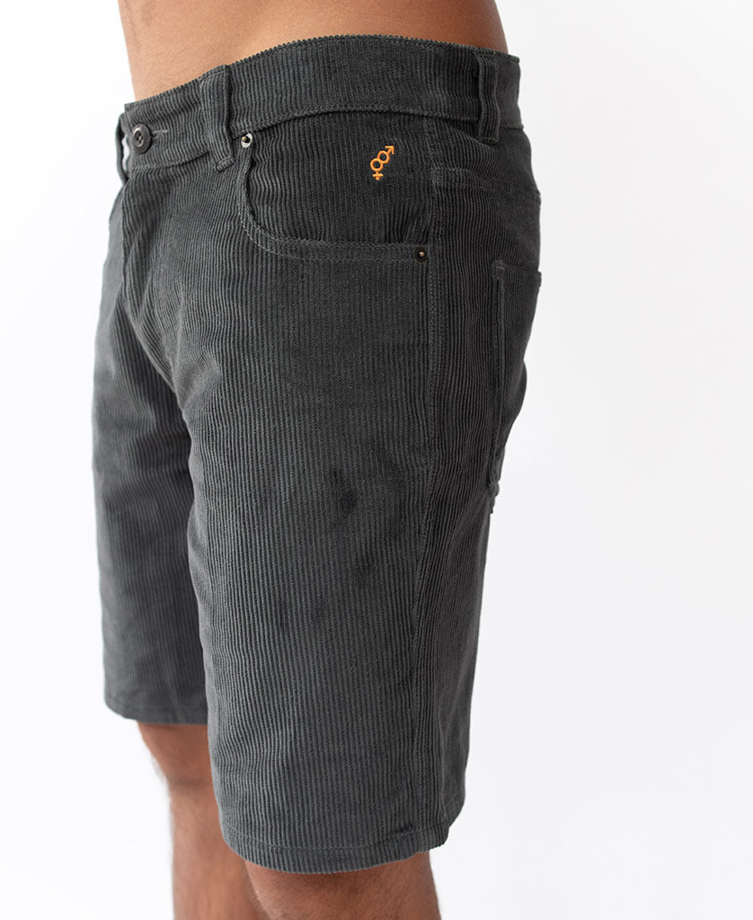 Model wearing Golden Breed Floyd Cord Walkshort in Wash Black, 100% cotton corduroy with a structured waist and orange logo near the front pocket, shown waist to above knee against a white background.