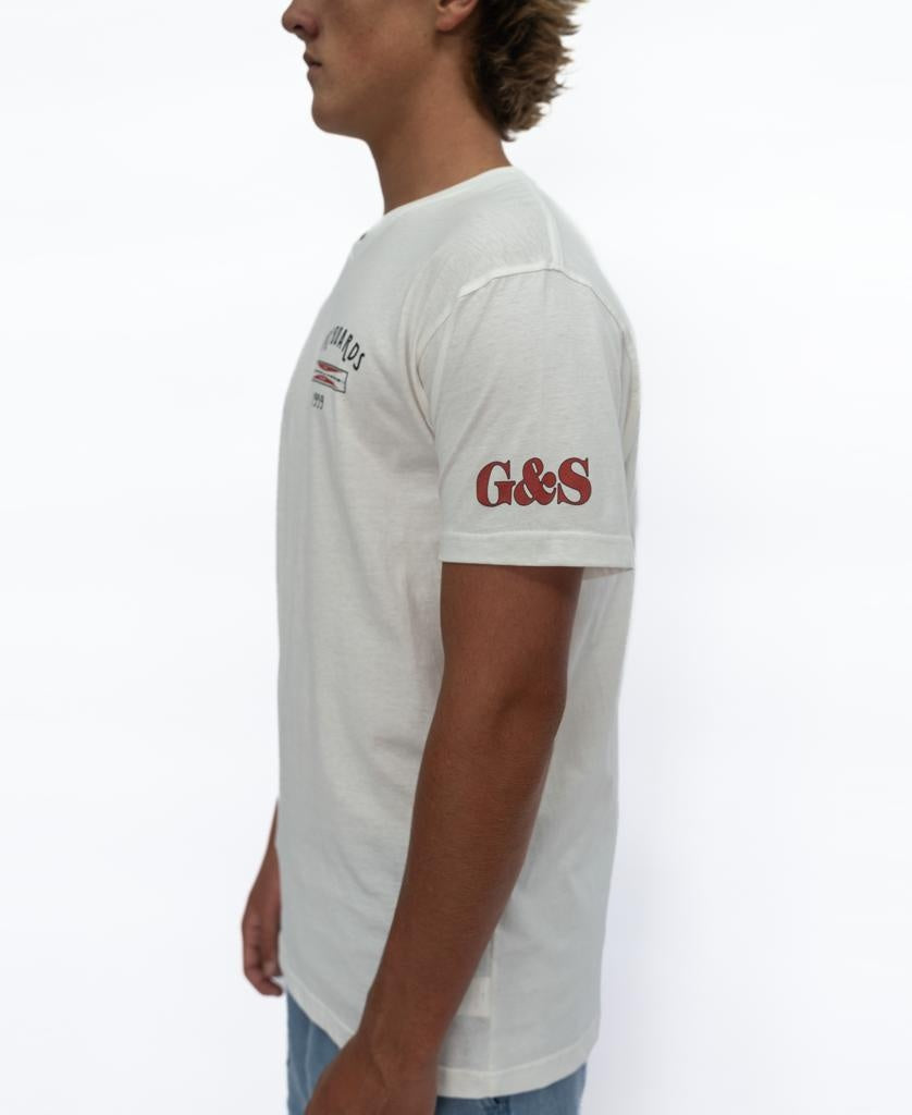 A person wears the G&S Surfboards Tee in Off White by Gordon & Smith, featuring red “G&S” on the left sleeve, shown from the side against a white background—ideal for classic surfboard style fans.