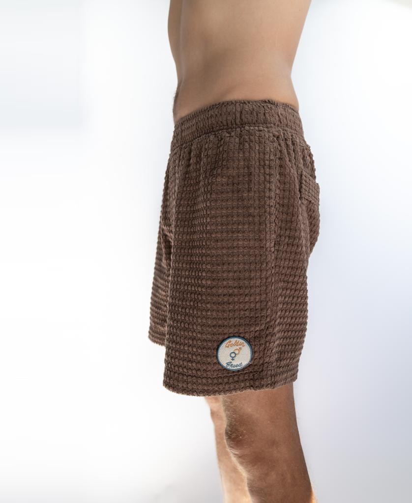Model wears Golden Breed’s El Shorto Walkshort in Wash Brown, featuring a textured finish, elastic waist, and circular patch on the lower side, shown waist to mid-thigh in side profile against a plain background.