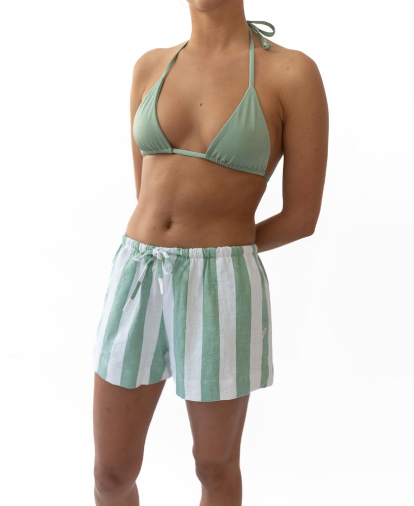 A person stands against a white background wearing Golden Breed’s Molly Short in Moss/White and a light green bikini top.