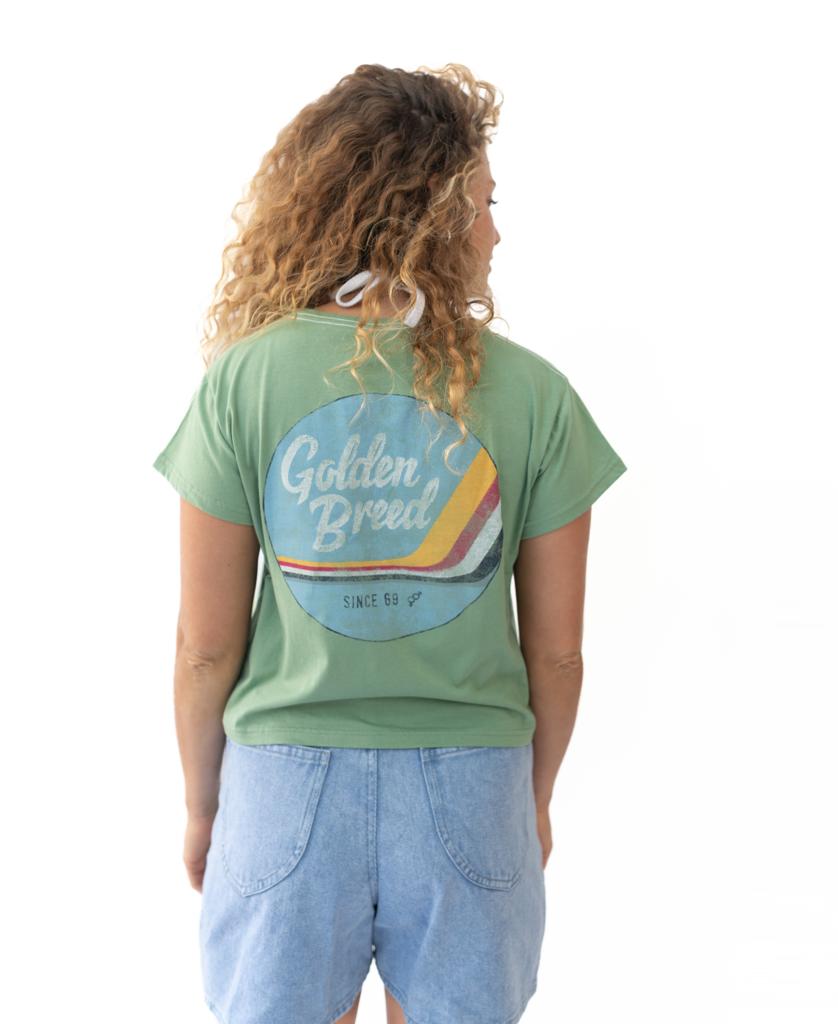 A person with curly hair, seen from behind, wears a soft cotton Moss Hattie Tee by Golden Breed and light blue denim shorts against a plain white background.