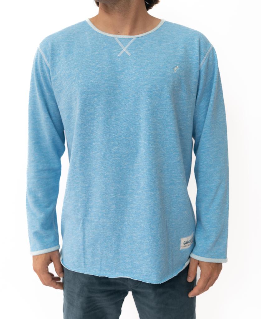 A person in the Golden Breed Classic Rag Top | Sky Marle, a light blue long-sleeve shirt with white stitching, captures a classic surf look against a plain white background.