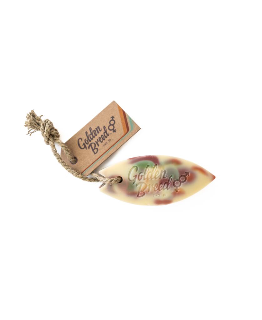 The Dindi Naturals Surfboard Soap on a Rope features a multicolored, surfboard-shaped soap with quality saponified oils, complete with rope and a branded cardboard tag.