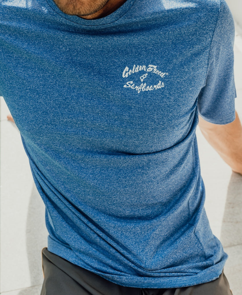 Wearing the Golden Breed Nemo S/S Rash Shirt in Blue Marle, a person relaxes with one arm on the ground, enjoying quick-drying comfort.