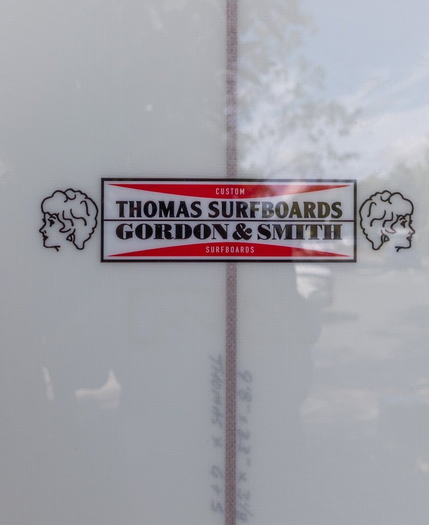 Close-up of the Gordon & Smith G&S X Thomas Longboard 98 logo sticker, showing two illustrated side profiles—honoring noseriding tradition and modern performance.