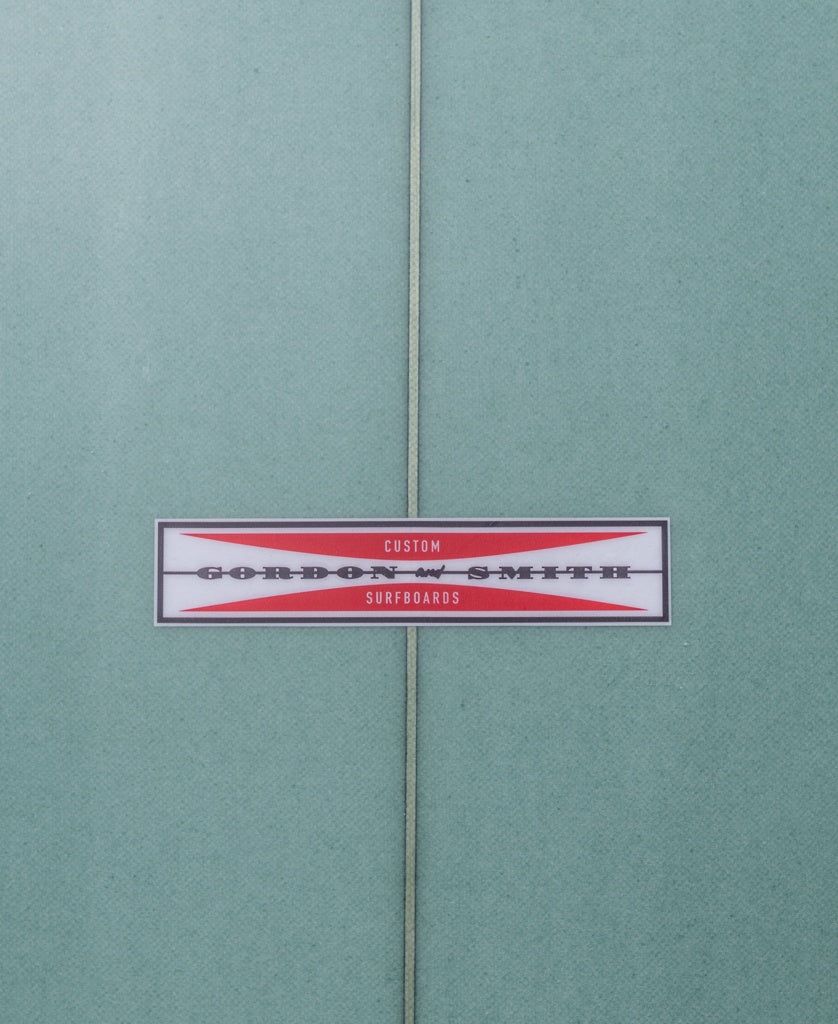 Close-up of the Gordon & Smith G&S Mid length Malachite Green 76 surfboard, featuring a centered label on a white and red background—an ideal all-rounder for versatile wave riding.