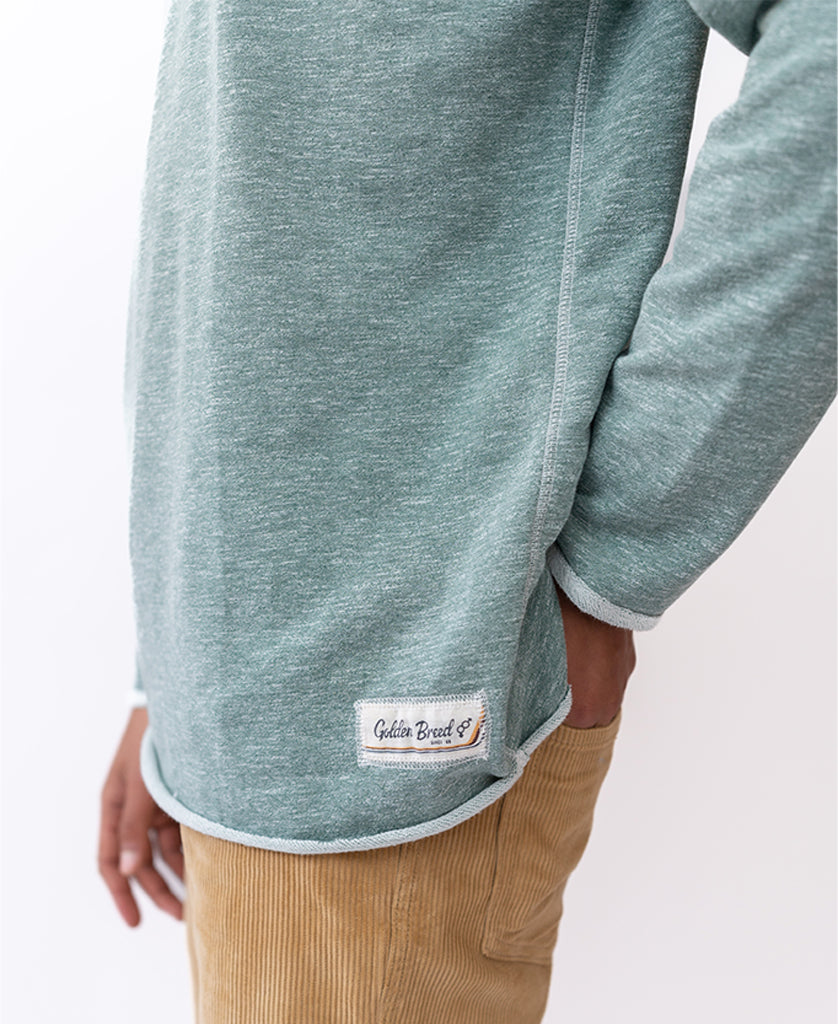 A person wears the Golden Breed Classic Rag Top in Surf Green Marle with tan corduroy pants, featuring a subtle Galita Beach label at the hem for a retro-inspired look.