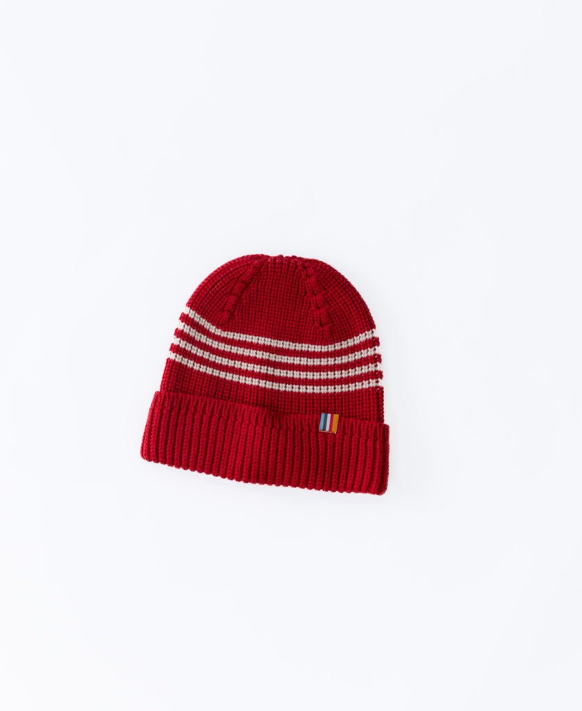 The Beach Boy Wool Beanie in red by Golden Breed features white horizontal stripes and a small multicolored tag on the folded brim, shown on a white background.