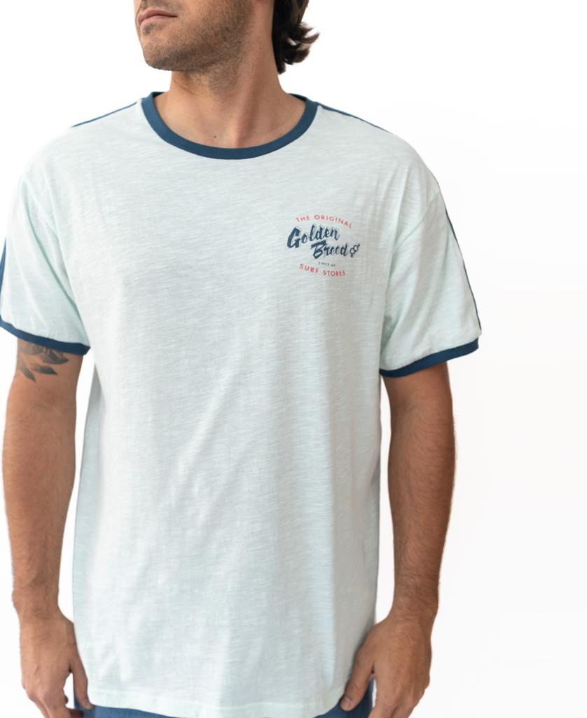 A man wears the Golden Breed Break Ringer Tee | Ice—a light blue 100% cotton shirt with dark blue trim and logo—standing against a white background. Designed in Australia for comfort and style.