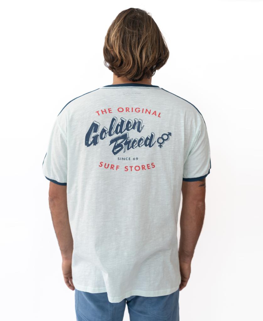 A person with shoulder-length hair, seen from behind, wears the Golden Breed Break Ringer Tee | Ice—made from 100% cotton and featuring The Original Golden Breed Surf Stores printed on the back.