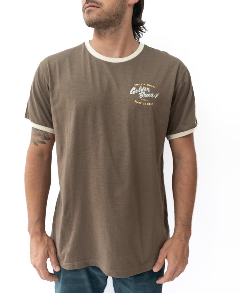 A man wears the Golden Breed Break Ringer Tee in Wash Brown, made from 100% cotton with a white collar, sleeve trim, and a small chest logo, standing against a plain white background.