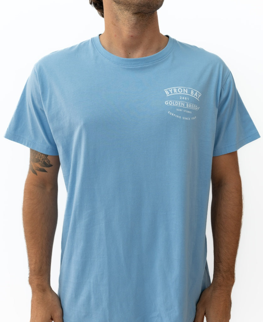 Someone wearing the Golden Breed Byron Boards Tee in Azure Blue, featuring a left-chest logo—ideal for relaxed Surf Town vibes.