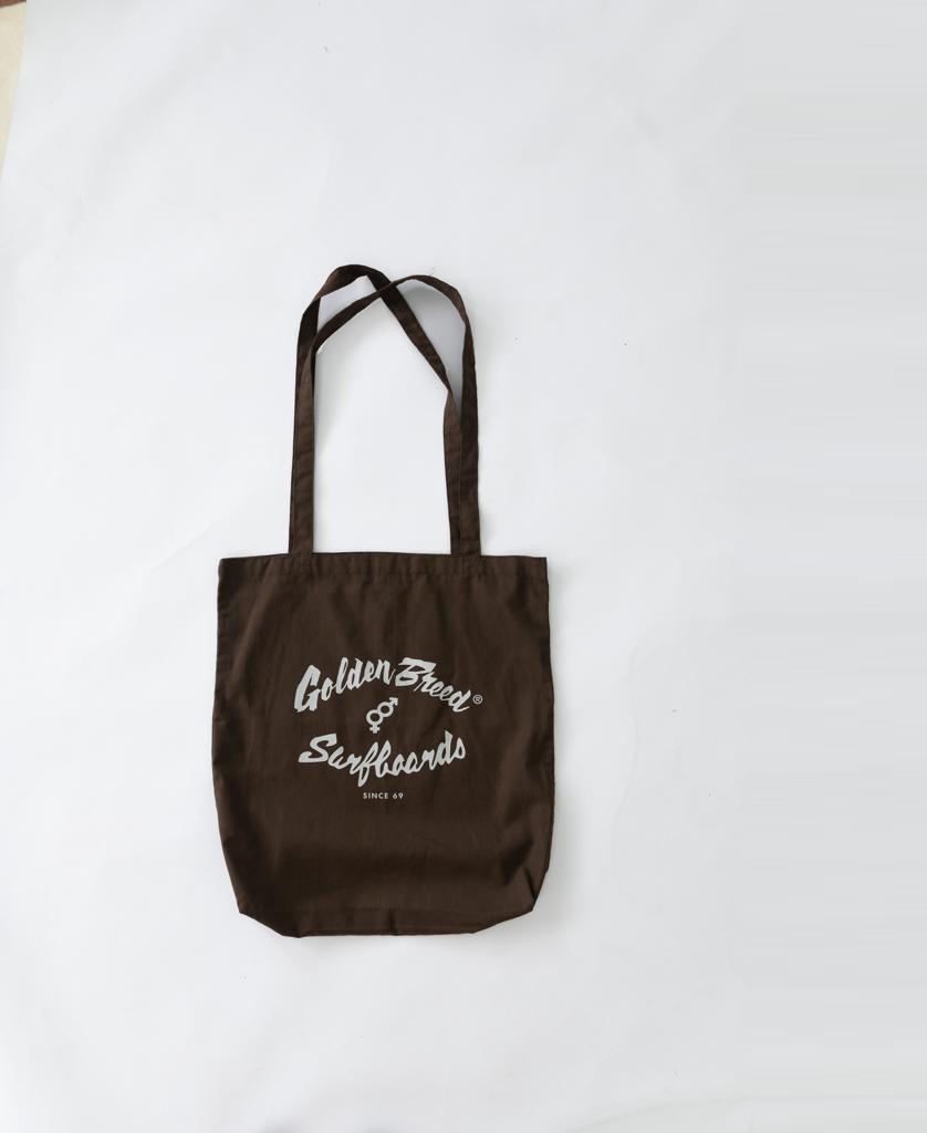 The Surf Logo Tote Bag | Brown by Golden Breed, featuring a white logo and made of cotton, is shown on a plain white surface.