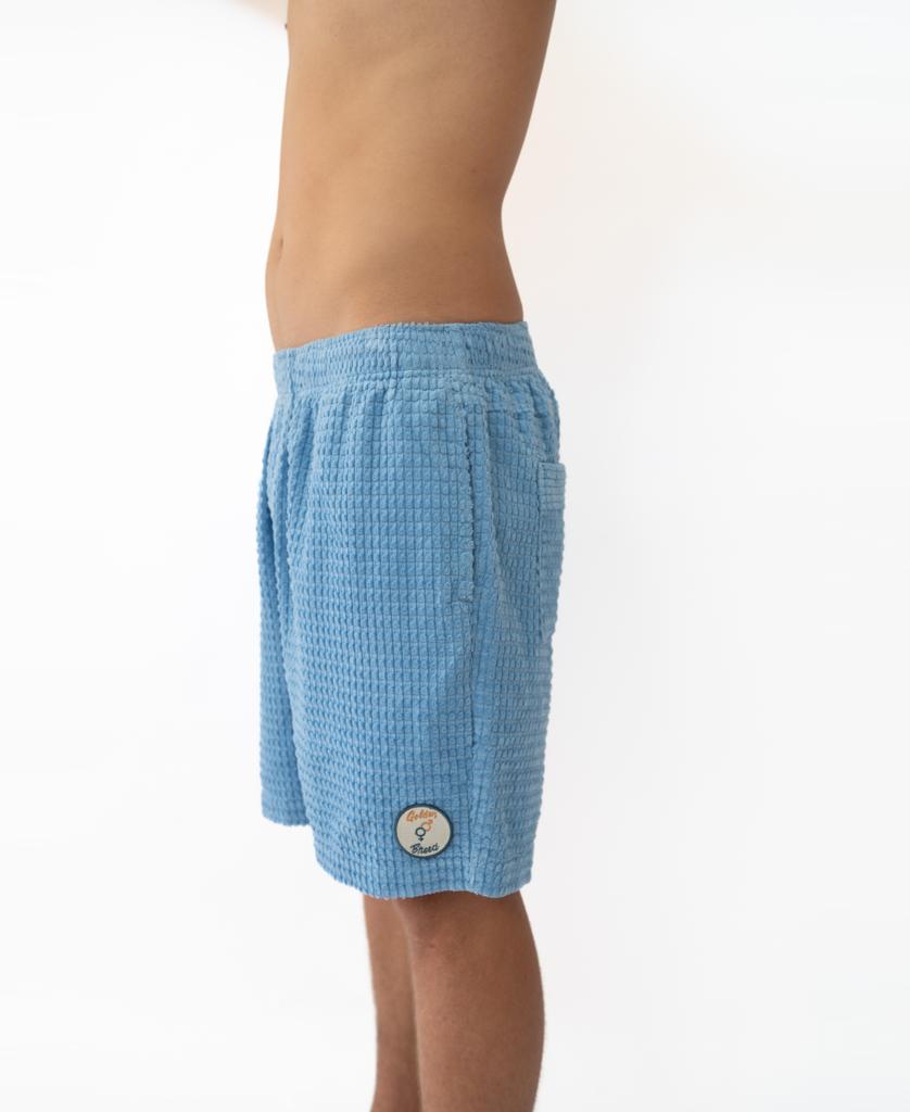 A person in profile wears Golden Breed El Solito Walkshort in Azure Blue, crafted from soft cotton cord material with an elastic waist and a small circular patch near the hem.