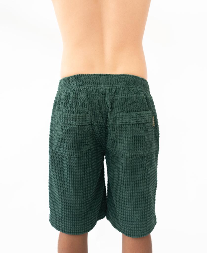 A person is shown from the back wearing Golden Breeds El Solito Walkshort in Ivy Green, featuring a textured finish, elastic waist, and two back pockets, standing against a plain white background.