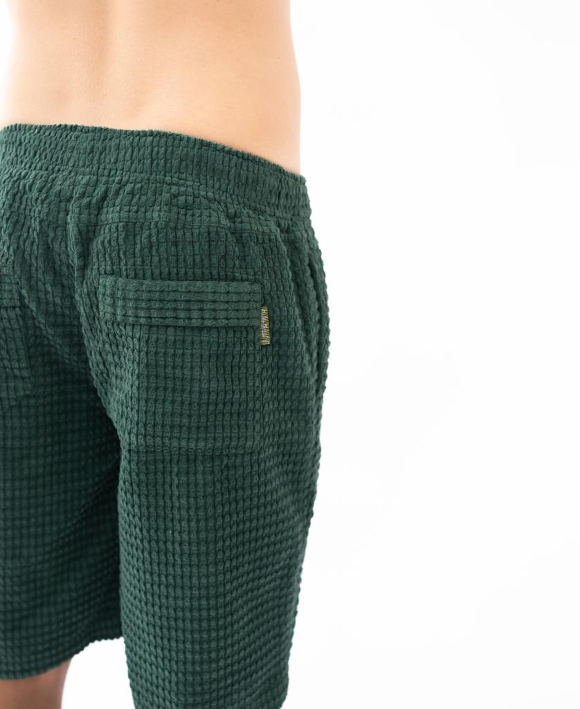 A person wears the Golden Breed El Solito Walkshort in Ivy Green, made from chunky cotton cord with an elastic waist and visible back pocket, shown from the waist down against a white background.