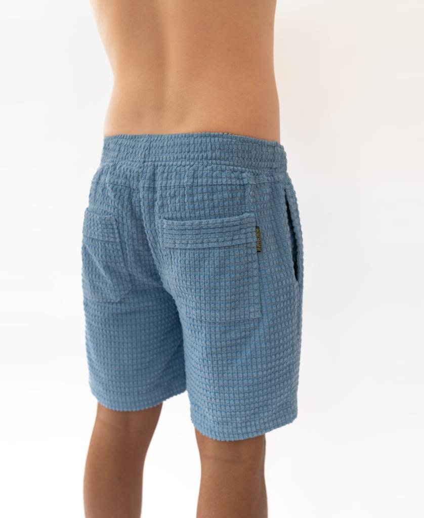 A person wearing Golden Breed El Shorto Walkshort in Azure Blue, featuring an elastic waist and two back pockets, is shown from the waist down and photographed from behind against a plain background.