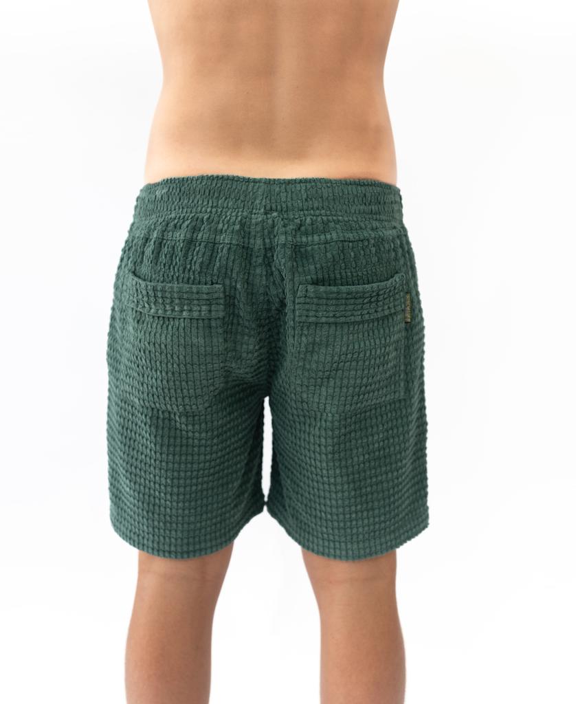 A person faces away from the camera wearing Golden Breeds El Shorto Walkshort in Ivy Green, featuring an elastic waist, chunky cotton cord, and two back pockets, set against a white background.