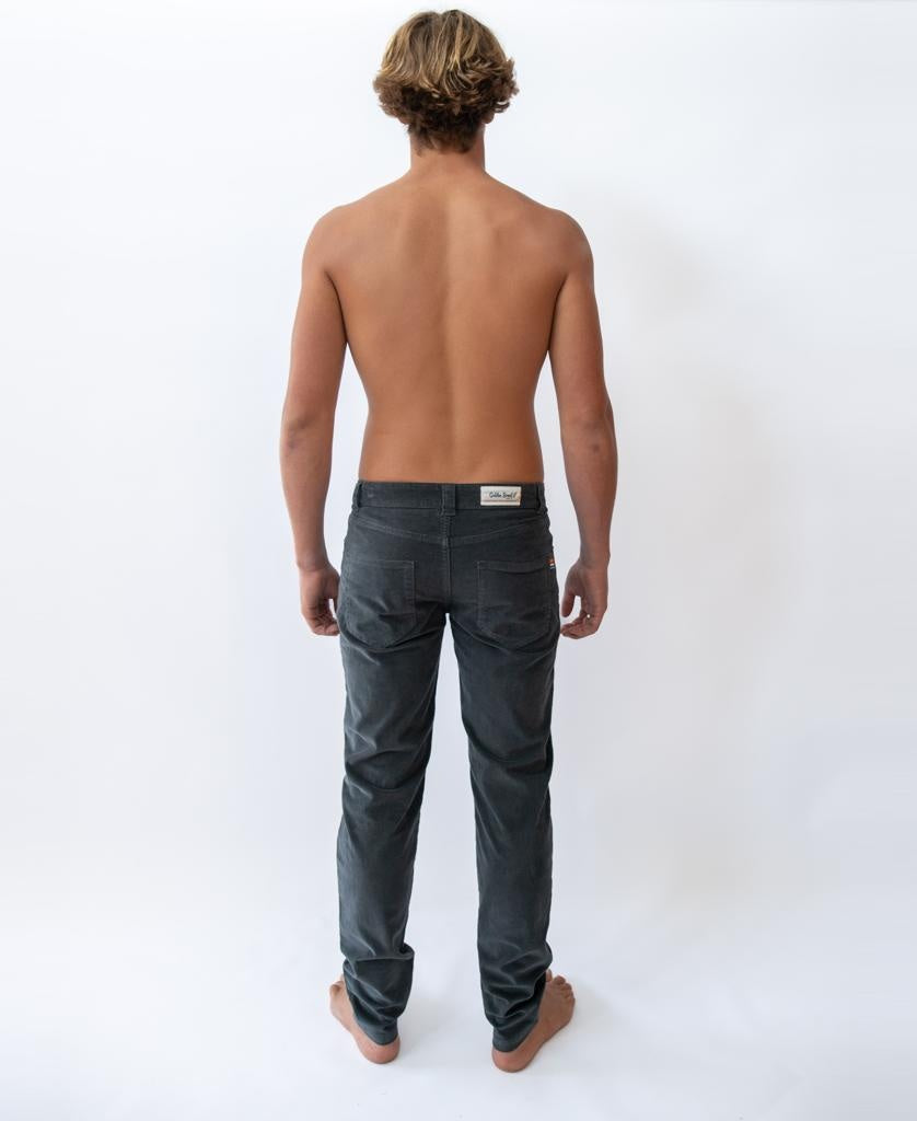 A shirtless person stands barefoot facing away from the camera, wearing Wash Black Felix Stretch Cord Pant by Golden Breed against a plain white background.