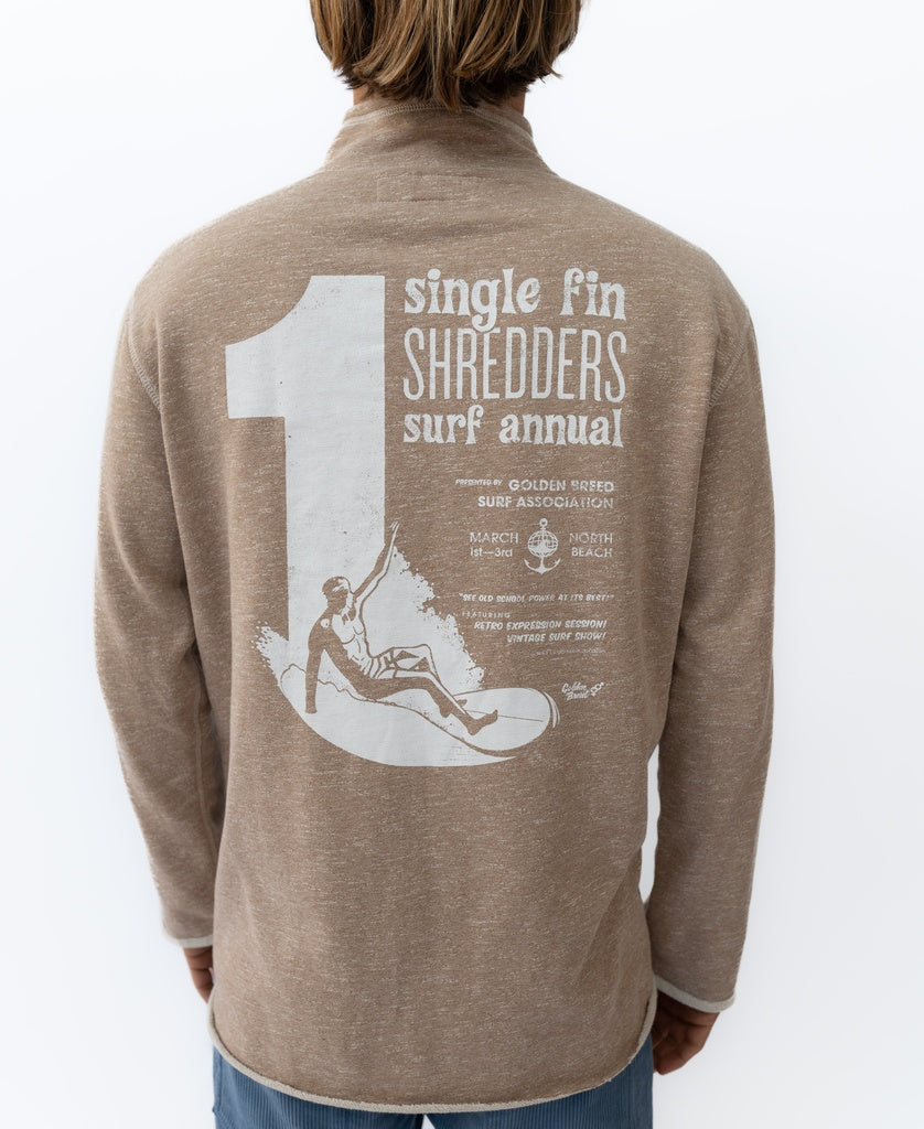 Someone wears the Golden Breed Fin 1/4 Zip Rag Top in Mocha Marle, featuring a large 1 and Single Fin Shredders Surf Annual graphic, event details, and a surfer illustration—crafted from cozy French Terry for comfort.