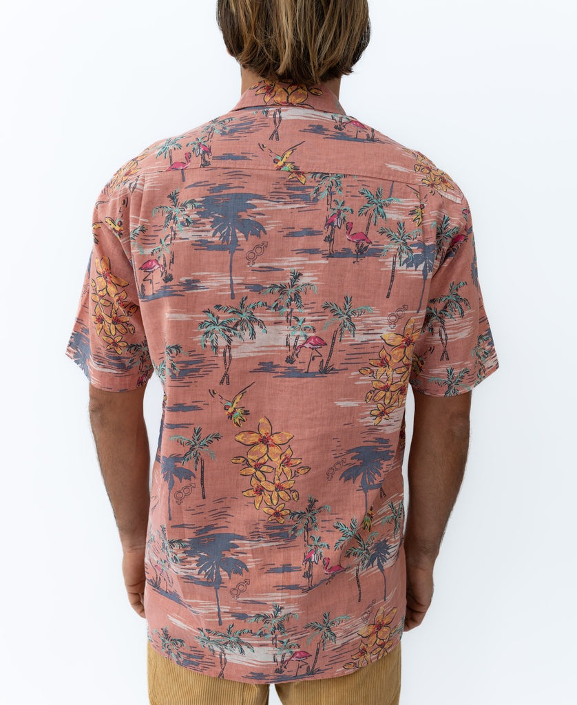 A man with light brown hair is seen from behind wearing the Golden Breed Flamingos Shirt | Rose— a short-sleeve, pink tropical print linen-blend shirt featuring palm trees and flowers, paired with tan shorts.