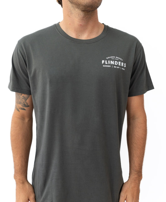 A man wears the Flinders Old School Tee | Wash Black by Golden Breed, a plain dark grey 100% cotton shirt with FLINDERS and small white text on the left chest. His face is partially out of frame.