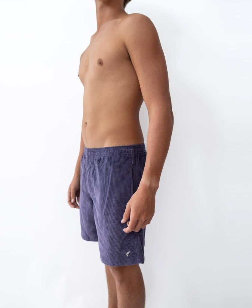 A shirtless person stands sideways against a plain white background, wearing Golden Breeds Floyd Cord Elastic Walkshort in Port.