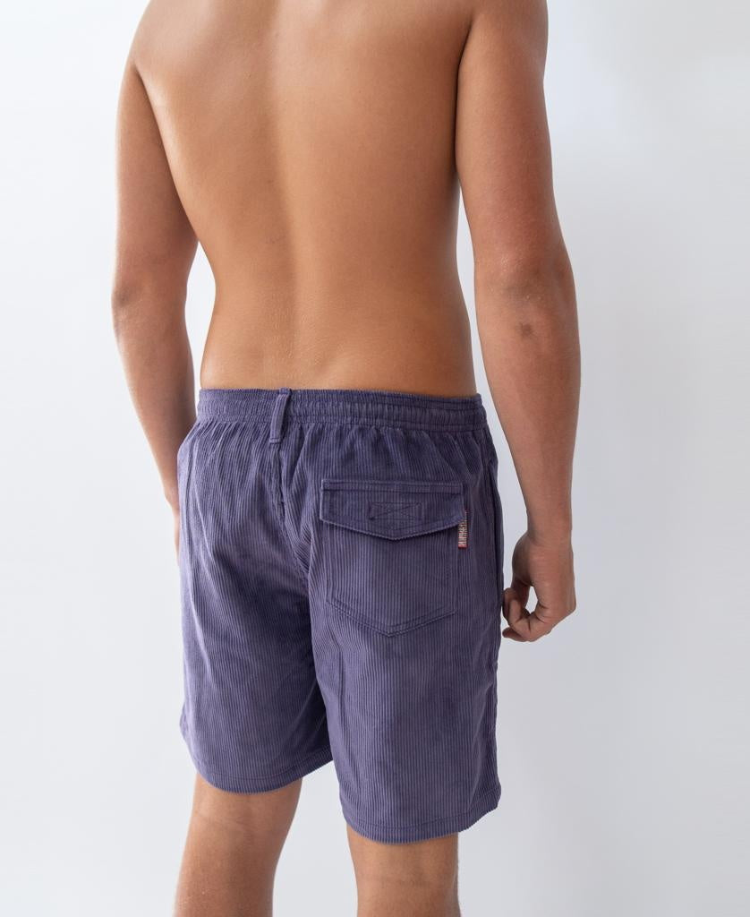 A person stands with their back to the camera, wearing Golden Breed Floyd Cord Elastic Walkshorts in Port, featuring an elastic waistband and a back pocket. The persons upper body is bare.