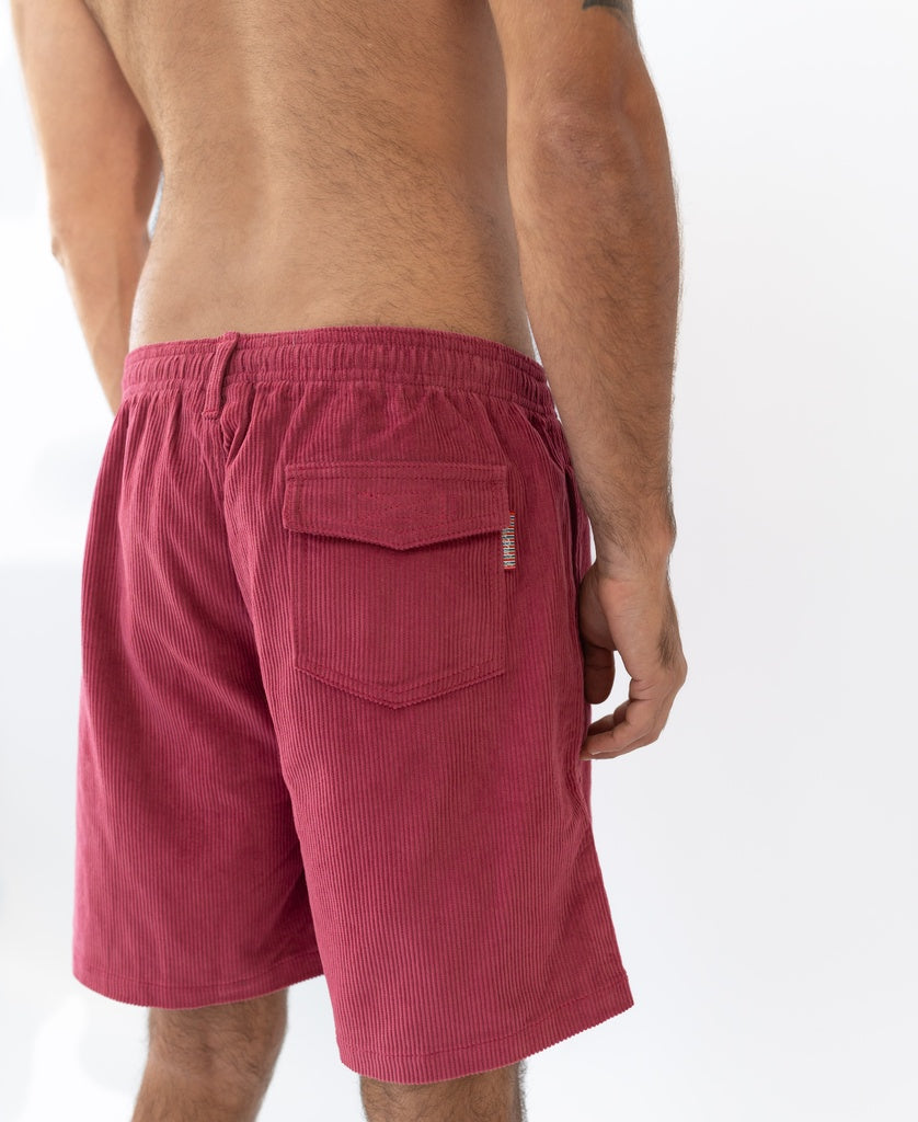 A man stands with his back to the camera, wearing Golden Breeds Floyd Cord Elastic Walkshort in Scarlet, featuring an elastic waist and a right-side flap pocket.