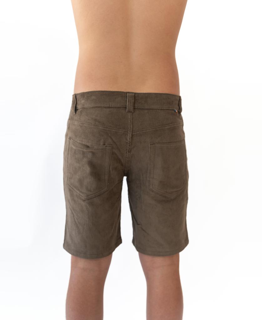 A person faces away from the camera wearing Golden Breed’s Floyd Cord Walkshort in Wash Brown, featuring a structured waist and no shirt, set against a white backdrop.