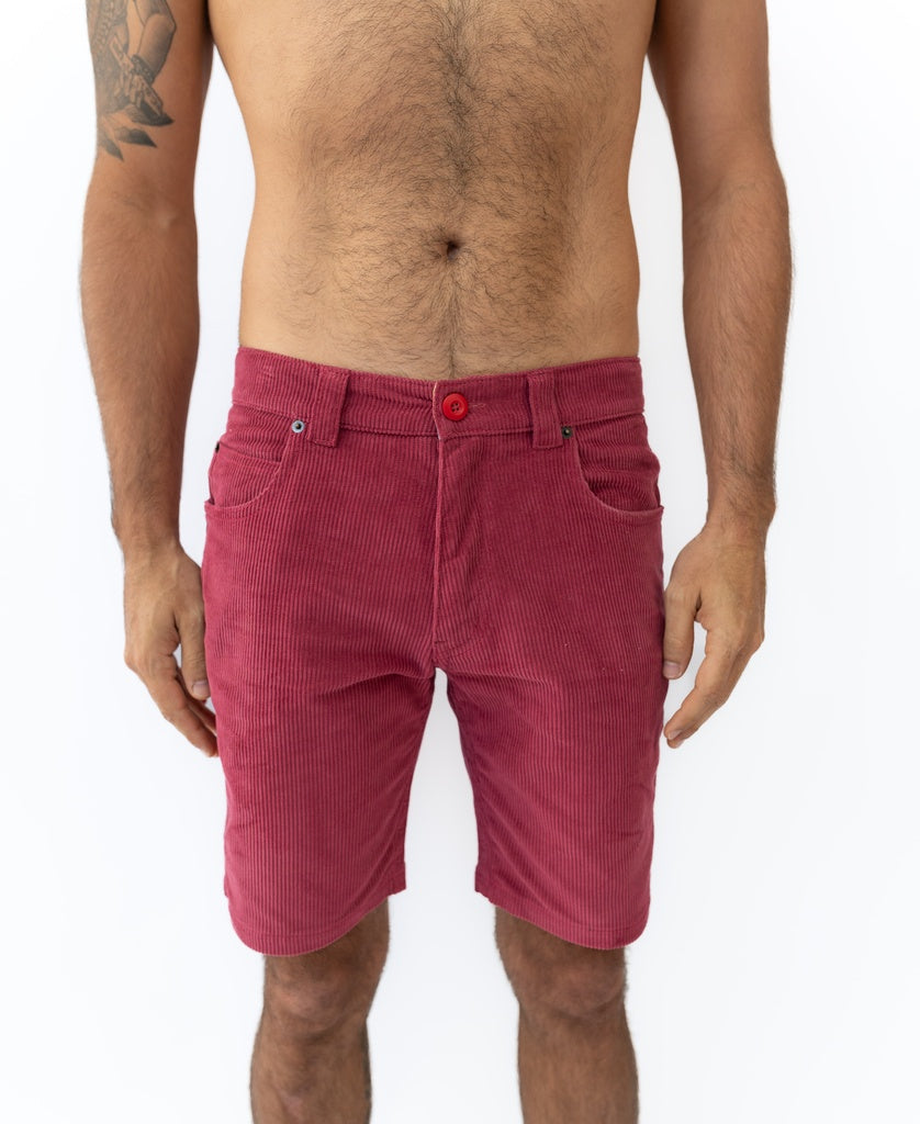A man models Golden Breeds Floyd Cord Walkshort in Scarlet, featuring a structured waist, against a plain white background, showcasing his torso and legs.