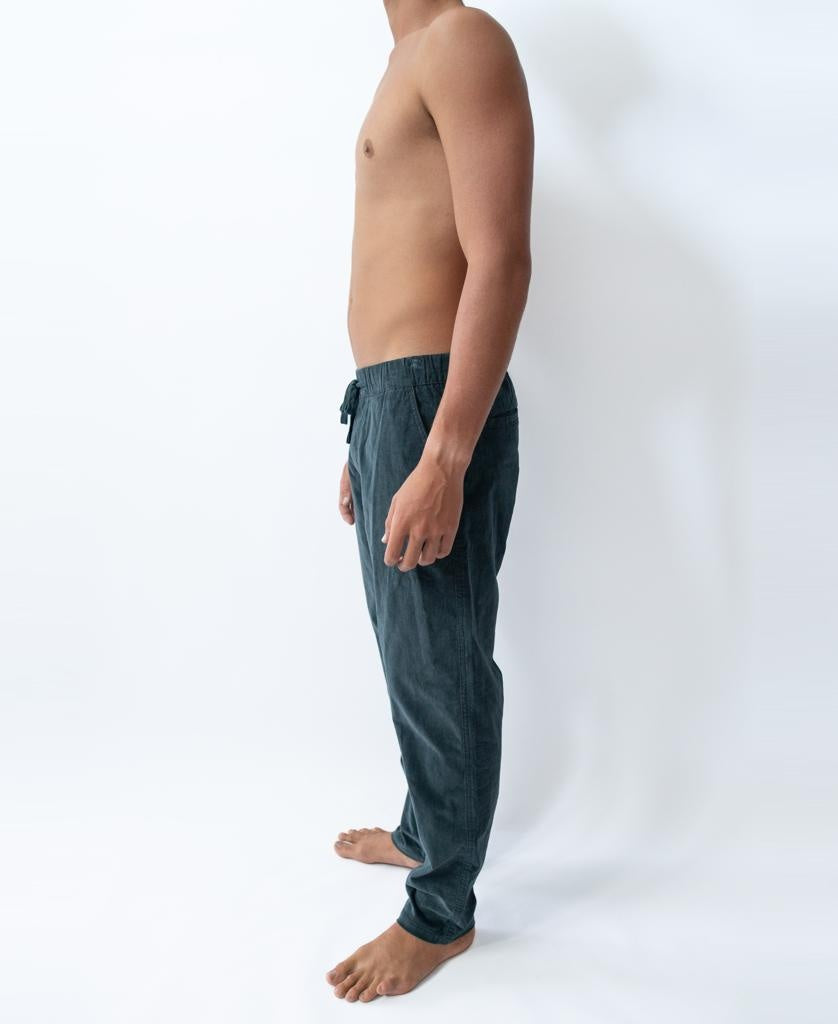 A shirtless person stands sideways, barefoot, wearing Golden Breeds Fred Stretch Cord Pant in blue against a plain white background.