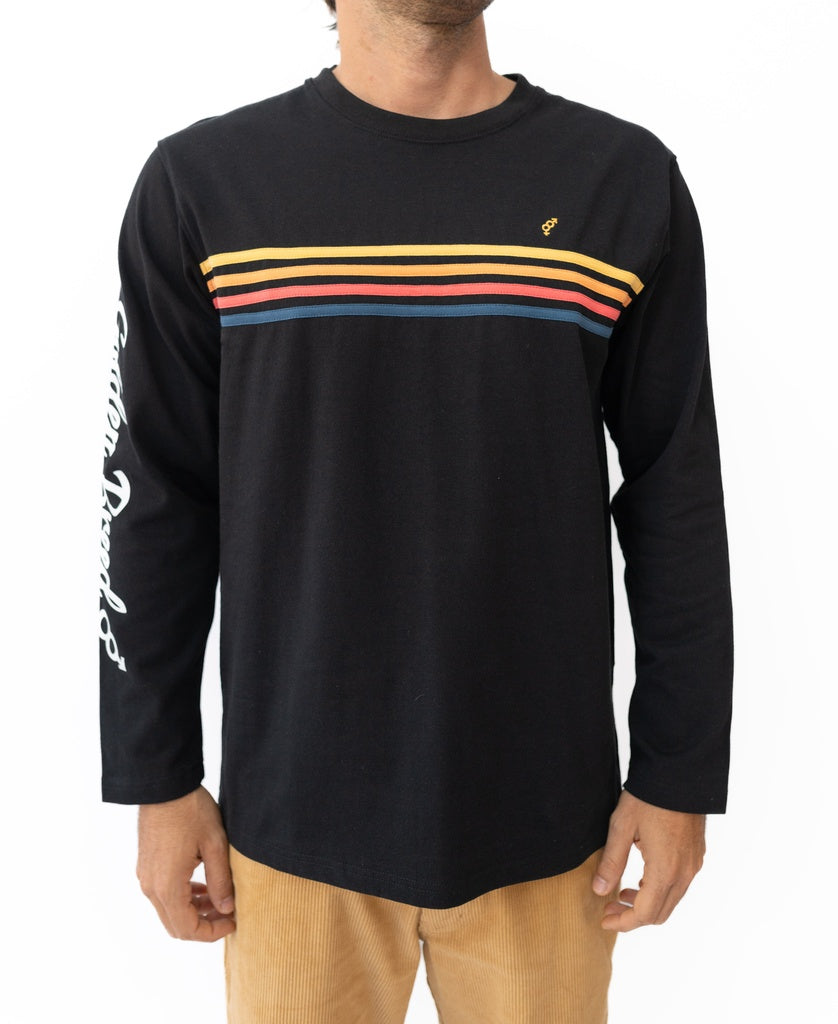 Sporting Golden Breed’s Heavy Island Long Sleeve Tee in black with colorful stripes and white sleeve text, paired with tan pants, this look channels a classic Cali surf vibe.