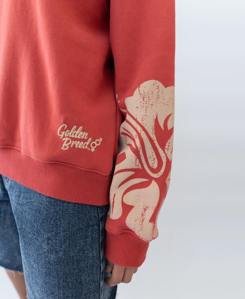 A person wears the Golden Breed Hibiscus Sweat in Wash Red/Beige, made from 100% cotton fleece with bold text and a large floral sleeve graphic, paired with blue denim shorts.