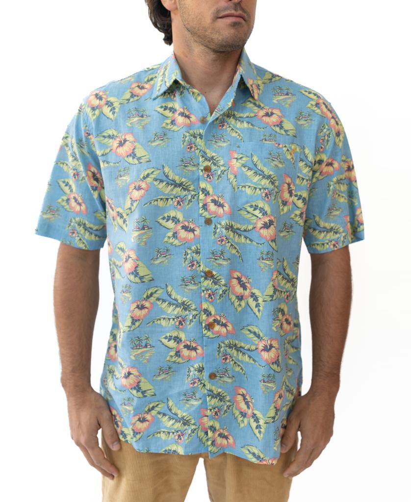 A man wears the Golden Breed Howe Shirt in azure blueβan oversized-fit Hawaiian shirt with yellow and red florals, made from a comfy cotton/linen blendβand beige pants, standing against a white background.