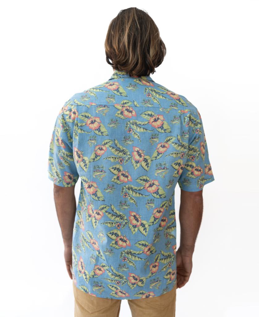 A person with shoulder-length hair stands with their back to the camera, wearing the Golden Breed Howe Shirt in Azure Blue and tan pants against a white background.