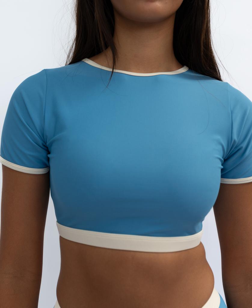 A person wearing the Golden Breed Indie Crop Tee Retro in Azure/Off White stands against a plain background.