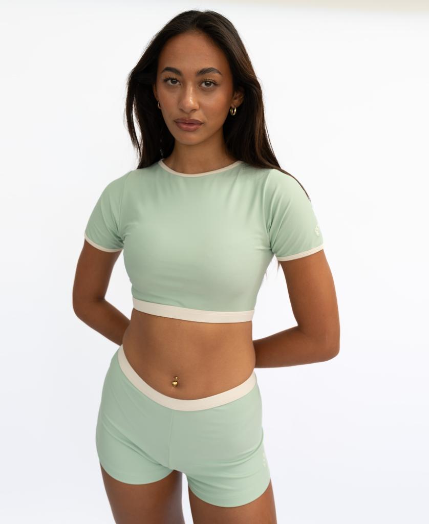 A woman poses against a white background wearing the Golden Breed Indie Crop Tee Retro in Moss/Off White, looking directly at the camera.