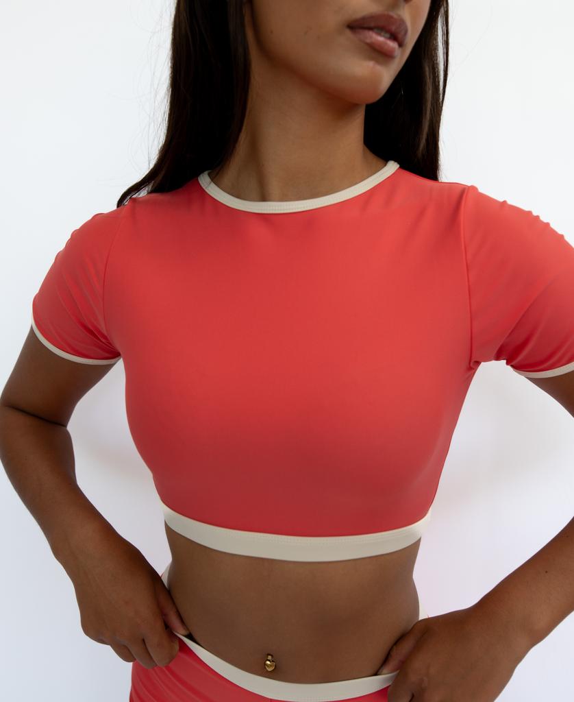 A woman models the Golden Breed Indie Crop Tee Retro in Surf Red with Off White trim, hands on hips against a white background, capturing laid-back retro surf style.