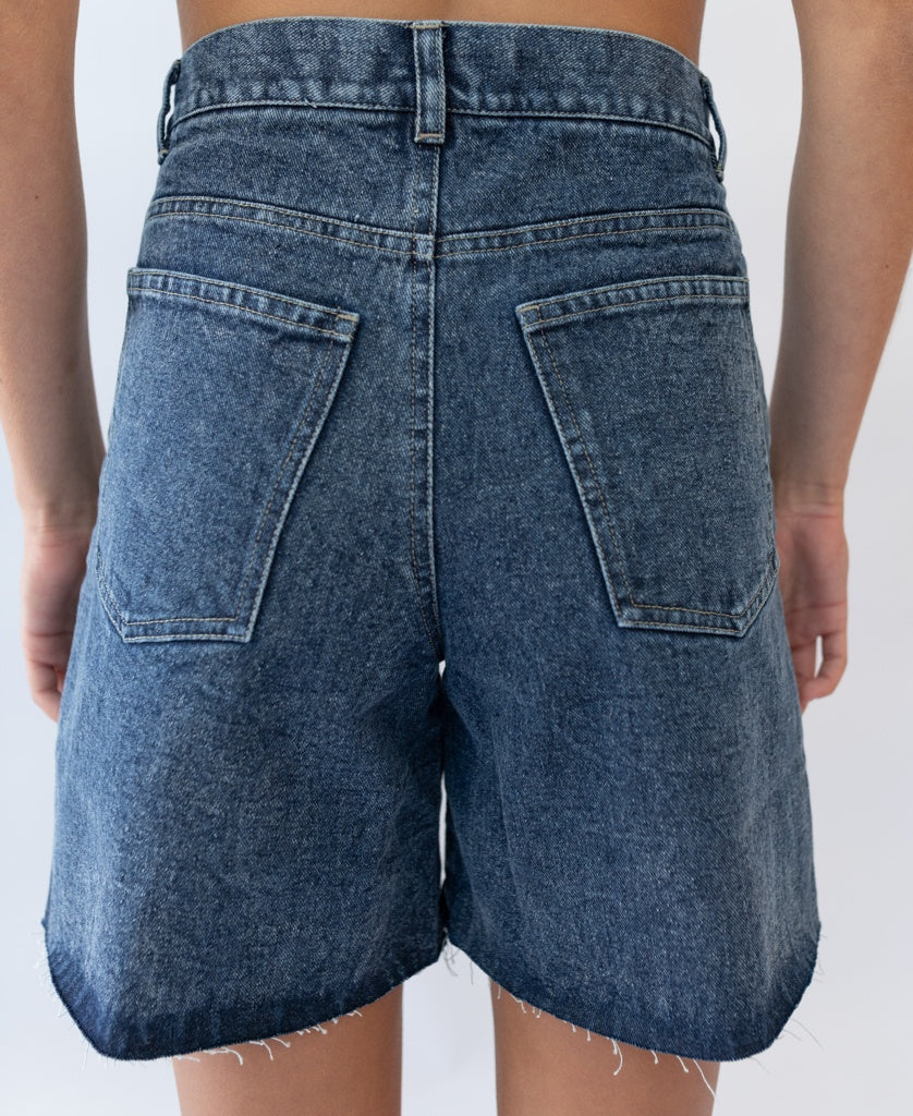Back view of a person wearing Golden Breed’s Izzy Short | Dark Blue, featuring a high waist, raw hems, and two large back pockets.